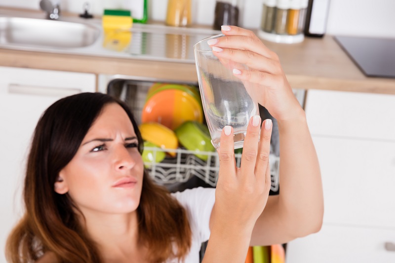 Woman Looking At spotty glass from dirty dishwasher